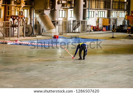Worker stretching the red white warning tape to the pole at construction site.Red and white Hazardous restricted area tape at construction area of factory to mark territory works.