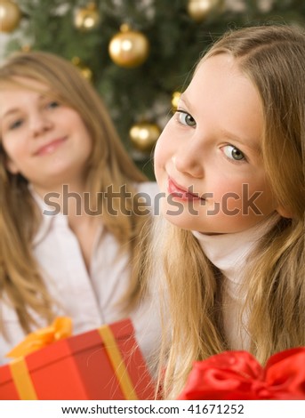 Two lovely, blonde hair girls next to the christmas tree with golden glass-balls.