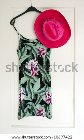 Sexy flowered summer dress and pink hat on hanger on white door