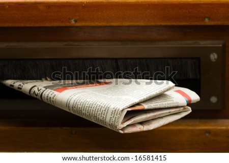 Very high resolution shot of newspaper coming in the mail box in a wooden door.