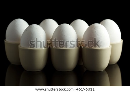 white chicken eggs in egg-cups on black reflecting background