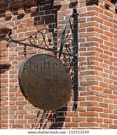 Blank, dark, shop sign hanging in a wrought iron bracket from a brick wall