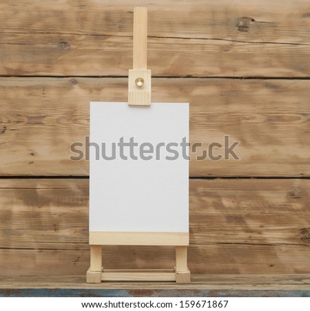 blank canvas on wooden easel against wooden background