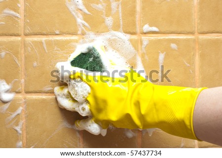 hand in yellow rubber glove holding soapy cleaning sponge