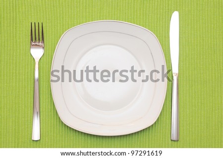 Empty dish, knife and fork and green napkin on wood table