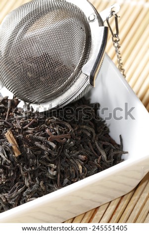 black tea leaves in white bowl with strainer on bamboo mat