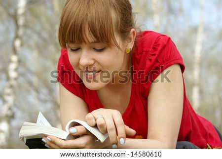 Young girl lying with a book on spring grass in a park and  reading