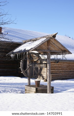 Old wooden house with draw-well in front. winter