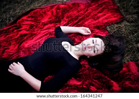 Pale woman in black dress lying on red carpet