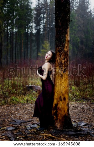Pale woman in purple dress lying upon a tree