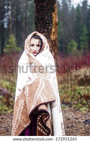 Beautiful woman in warm blanket in forest