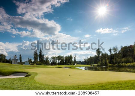 The sun shining over a golf course lined with buildings and trees