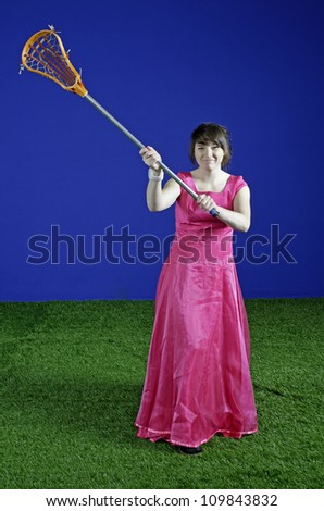 A teenage girl in a pink prom dress is ready with her lacrosse stick to defend her end of the field.