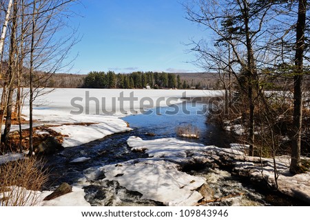 Stream leading into a ice covered lake on a warm spring day as the snow melt runs into the lake.