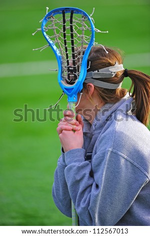 High school girls lacrosse player waits her turn to get into the game as she watches from the side lines.