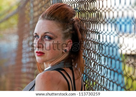 Young woman looks back over her shoulder as she leans back against the chain link fence.