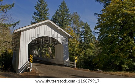 1920\'s era covered bridge on the back roads in America with a fresh coat of white paint under the contrast of blue autumn skies and the trees in the area begin to change their colors.