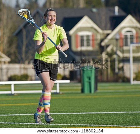 Teen age girls lacrosse player passing the ball as she runs down the field.
