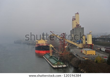 A ship is docked at a rail road yard with fog rolling in the background.