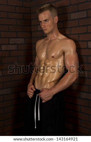 A handsome young physically fit man leaning against a brick wall showing off his hard earned abs.
