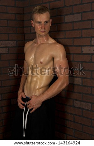 A physically fit man leaning against a brick wall showing off his hard earned abs.