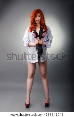 Sexy redhead wearing a men`s shirt over her sexy lingerie and posing on gray background