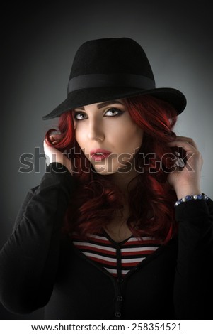 Studio portrait of a young redhead woman posing with a black fedora hat