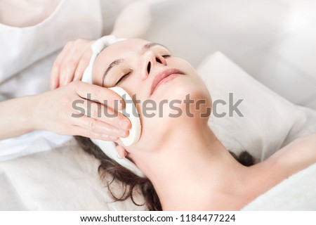 Hands of female beautician cleanses the skin. Facial skincare. Beautiful caucasian woman on a cosmetology procedure. Visit to the beauty salon