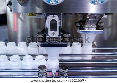medicine pill capsules are filling in the white plastic bottle on production line machine conveyor at the medical factory.