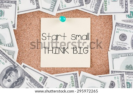 Yellow sticky reminder on corkboard with START SMALL THINK BIG message with border made of 100 US dollars