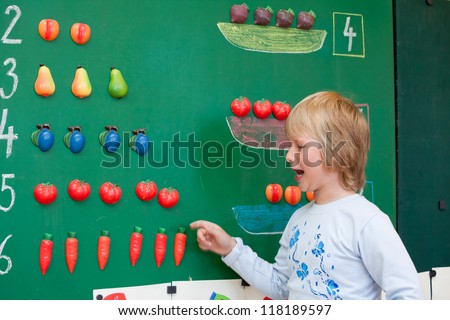 Fresh first year schoolgirl student is standing before blackboard during mathematics lesson.