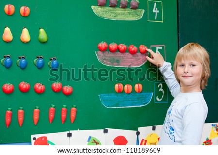 Fresh first year schoolgirl student is standing before blackboard during mathematics lesson.