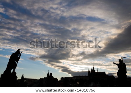 Silhouette of statues standing on Charles Bridge with Little Quarter and Prague Castle on the background.