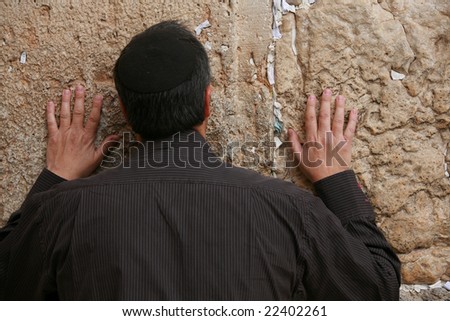 Praying men is touching Western Wall filled by wishes in Jerusalem.