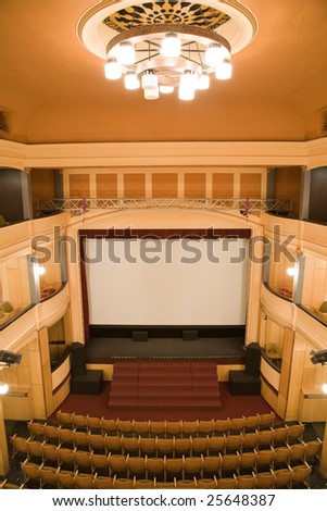 Empty old theater auditorium with arc line of chairs, main chandelier and stage with silver screen. Ready for adding your own picture.