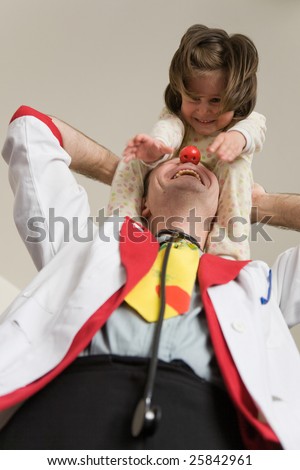 Clown-doctor : girl with stretched hands is sitting on shoulders of red nose clown and both are smiling and joking.