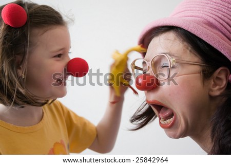 Clown-doctor : smiling girl is joking and beating clown with red nose by yellow chicken toy.