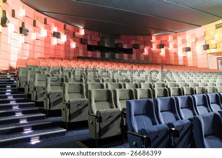 Empty new cinema auditorium with rows of blue, gray and red chairs and illuminated stairs.
