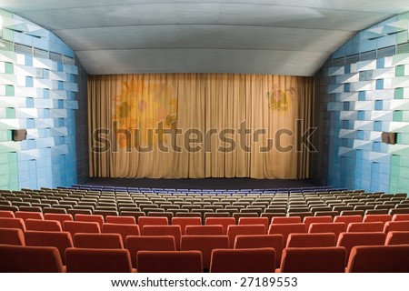 Empty cinema auditorium with line of chairs and stage with silver screen.
