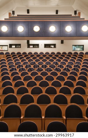 Interior of modern cinema auditorium with balcony and line of brown wooden chairs.