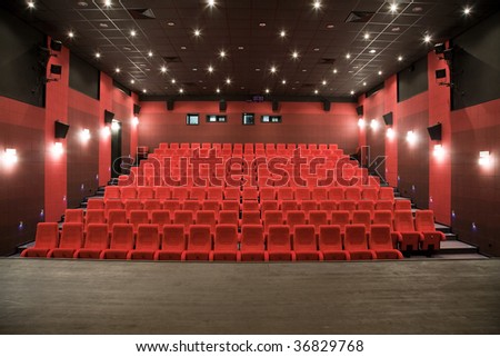 Interior of cinema auditorium with stage and lines of red chairs.