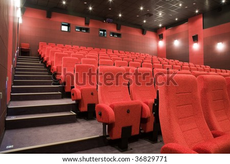 Interior of cinema auditorium with stairs and lines of red chairs.