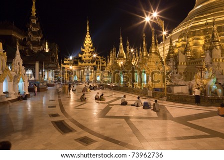 The biggest Buddhist temple Schwedagon pagoda at night lighting with praying Buddhist people, Rangoon, Burma.