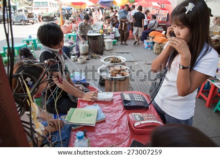 BURMA, RANGOON - FEBRUARY 13, 2011: People are making calls in local phone booth on street market.