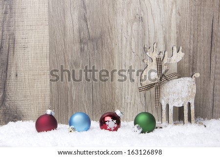 christmas decoration with wood background, snow, elk and christmas baubles red, blue, green