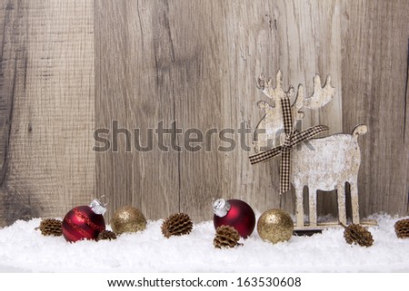 christmas decoration with wood background, snow, elk, christmas baubles gold and red and pine cones