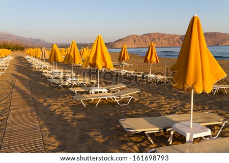 Sun beds and shade umbrellas early morning at a beach on Crete.