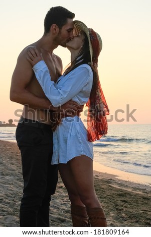 Happy young couple in their twenties, in wet cloths, embracing and kissing at the beach just before sunset.