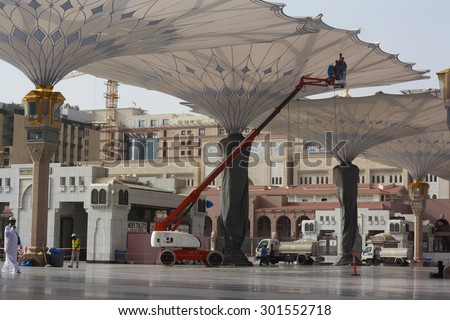 The employee was cleaning the giant umbrella.Taken on June 9.2015.in Prophet mosque Medina, Saudi Arabia
