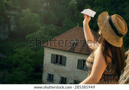 Woman in Hat with Paper Airplane on Balcony